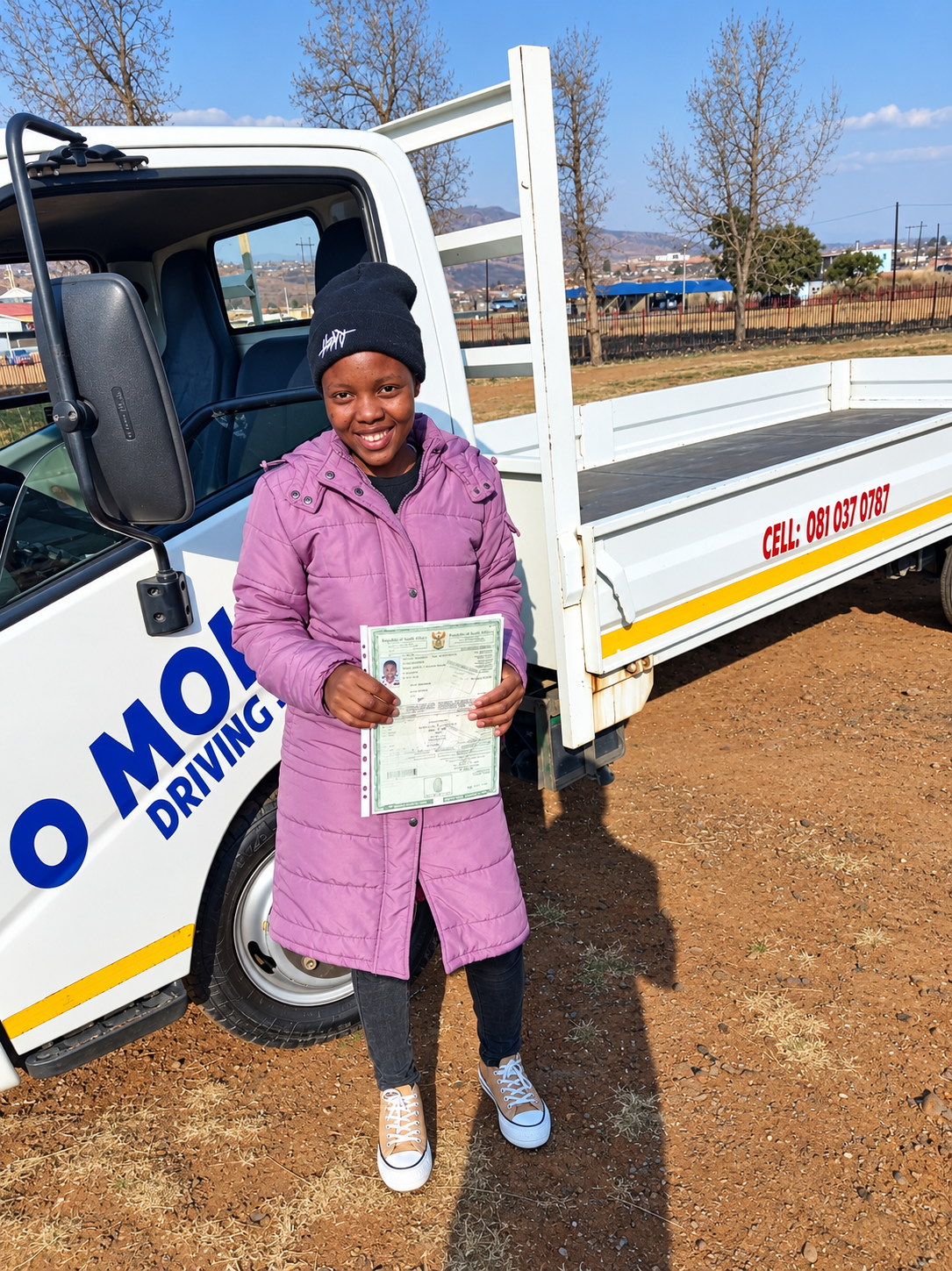 O Molemo graduate holding a driver licence next to the school vehicle